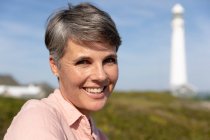 Portrait close up of a Caucasian woman enjoying free time relaxing on a beach near a lighthouse beside the sea on a sunny winter day smiling to camera — Stock Photo