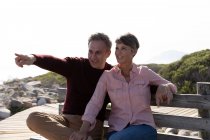 Vorderansicht eines erwachsenen kaukasischen Paares, das die freie Zeit auf einer Bank genießt und an einem sonnigen Tag lächelt — Stockfoto
