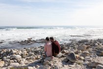 Vue arrière d'un couple adulte caucasien profitant de temps libre pour se détendre ensemble sur une plage au bord de la mer par une journée ensoleillée — Photo de stock
