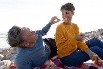 Vista frontale primo piano di una coppia caucasica adulta che si gode il tempo libero rilassandosi insieme su una spiaggia mangiando in una giornata di sole — Foto stock