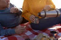 Вид спереди на взрослую кавказскую пару, наслаждающуюся свободным временем, отдыхая вместе на пляже, пьющую кофе в солнечный день — стоковое фото