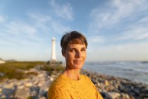 Porträt einer kaukasischen Frau, die an einem sonnigen Tag ihre Freizeit an einem Strand am Meer in der Nähe eines Leuchtturms genießt — Stockfoto