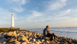 Вигляд дорослої кавказької пари, яка у сонячний день відпочиває разом на пляжі, обіймаючи разом біля моря біля маяка. — стокове фото