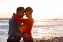 Side view of an adult Caucasian couple enjoying free time relaxing together on a beach embracing together beside the sea on a sunny day — Stock Photo