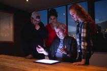Vista frontal de um grupo diversificado de criativos por uma mesa em uma sala de conferência de escritório, olhando para um computador tablet em uma discussão em uma reunião — Fotografia de Stock