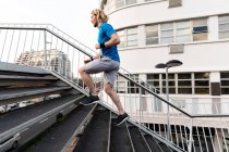 Seitenansicht eines jungen gutaussehenden athletischen kaukasischen Mannes, der auf einer Fußgängerbrücke in einer Stadt übt und die Treppe hinaufläuft — Stockfoto