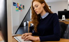 Vista lateral de una joven mujer caucásica que trabaja en una oficina creativa, usando una computadora, escribiendo . - foto de stock