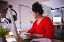 Бічний вид на молоду змішану расу жінку, яка працює в творчому офісі, сидячи за столом за комп'ютером. — стокове фото
