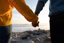 Средняя часть пары наслаждается свободным временем на пляже, держась за руки у моря в солнечный день — стоковое фото