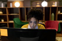 Frontansicht einer jungen kaukasischen Frau mit gemischter Rasse, die spät in einem modernen Büro arbeitet, an einem Schreibtisch sitzt und auf einen Desktop-Computermonitor starrt — Stockfoto
