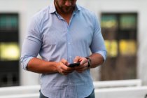 Front view close up of a young Caucasian professional man working late at a modern office, standing on the roof terrace using a smartphone — Stock Photo