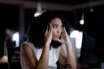 Nahaufnahme einer jungen Frau mit gemischter Rasse, die spät in einem modernen Büro arbeitet, am Schreibtisch sitzt, ihren Kopf hält und auf einen Desktop-Computermonitor starrt — Stockfoto