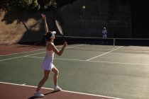 Вид сбоку на молодую кавказку и мужчину, играющего в теннис в солнечный день, женщину, бьющую по мячу — стоковое фото