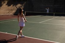 Veduta posteriore di una giovane donna caucasica e un uomo che giocano a tennis in una giornata di sole, prendendo una pausa sul campo — Foto stock