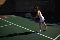 Vista lateral de la mujer jugando al tenis en un día soleado, preparándose para servir con una pared detrás de ella - foto de stock