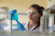 Primo piano di giovane studentessa universitaria che guarda chimica mentre pratica esperimento in laboratorio — Foto stock