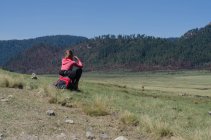 Rückansicht einer Wanderin, die bei klarem Himmel auf einem Felsen auf einem Feld sitzt — Stockfoto