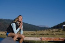 Улыбающаяся задумчивая женщина, сидящая на перилах против ясного голубого неба — стоковое фото