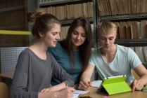 Estudantes universitários olhando para o computador tablet enquanto estudam na mesa na biblioteca — Fotografia de Stock