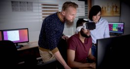 Колеги використовують гарнітуру віртуальної реальності під час роботи на комп'ютері в офісі — стокове фото