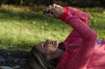Close up of female hiker using phone while lying on retaining wall in forest — Stock Photo