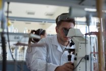 Estudiante masculino joven usando microscopio en laboratorio - foto de stock