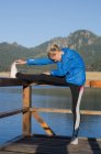 Giovane atleta donna che si allunga mentre si esercita sul molo contro il cielo limpido — Foto stock