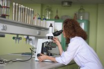 Вид збоку дівчини-підлітка, що практикує експеримент при використанні мікроскопа в лабораторії — стокове фото