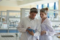 Male student showing clipboard to classmate while practicing chemistry experiment in lab — Stock Photo