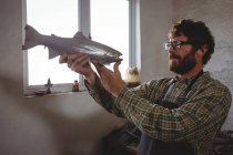 Внимательный мастер осматривает металлическую рыбу в мастерской — стоковое фото