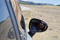 Close up of woman reflecting in side view mirror of car on sunny day — Stock Photo