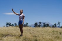 Полная длина женщины-туриста делает селфи, стоя на поле — стоковое фото