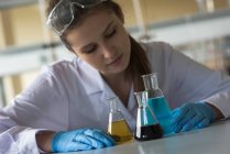 Студент коледжу дивиться на хімічні речовини в склянці на столі — стокове фото