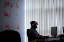 Executivo usando fones de ouvido de realidade virtual enquanto trabalhava na mesa no escritório — Fotografia de Stock