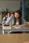 College students writing on book while sitting at desks during exam in classroom — Stock Photo