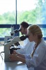 Estudantes universitários fazendo experiência em microscópio em laboratório na faculdade — Fotografia de Stock
