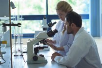 University students using digital tablet while doing experiment on microscope in laboratory at college — Stock Photo