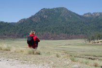 Rückansicht einer Wanderin mit Rucksack, die auf Feld gegen Berg sitzt — Stockfoto