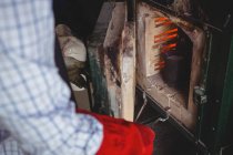 Mittelteil des Handwerkers, der Metall im Ofen in der Werkstatt erhitzt — Stockfoto
