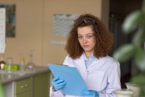 Portrait of teenage girl holding clipboard while standing in lab — Stock Photo