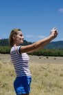 Vista laterale di un'escursionista sorridente che si fa un selfie in piedi sul campo — Foto stock