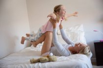 Side view of a Caucasian woman enjoying family time with her daughter at home together, lying on a bed in their bedroom smiling and lifting her above her — Stock Photo