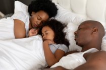 Blick aus der Vogelperspektive auf ein afroamerikanisches Paar und seine kleine Tochter im Schlafzimmer, die zusammen schlafend im Bett liegen — Stockfoto
