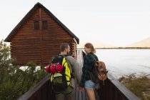 Передній вид на кавказьку пару добре проводить час у поїздці в гори, йдучи по мосту до хатини, тримаючись за руки. — стокове фото