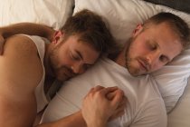 Высокий угол обзора крупным планом кавказских мужчин, расслабляющихся дома, лежащих в постели, обнимающихся и спящих вместе. — стоковое фото