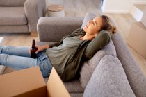 Caucasian woman spending time at home self isolating and social distancing in quarantine lockdown during coronavirus covid 19 epidemic, taking a break while doing DIY, resting on a sofa and drinking a beer. — Stock Photo