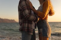 Mitte des Paares, das bei Sonnenuntergang auf einer Strandpromenade am Meer steht, einander gegenübersteht und sich umarmt. Romantisches Urlauberpaar am Meer — Stockfoto
