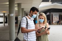 Vista frontale di una coppia caucasica in giro per le strade della città durante il giorno, indossando maschere contro l'inquinamento atmosferico e covid19 coronavirus, utilizzando i loro smartphone. — Foto stock