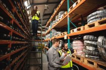 African American and Caucasian factory workers wearing a high vis vest and Caucasian male supervisor using laptop and checking stock. Workers in industry at a factory making hydraulic equipment. — Stock Photo
