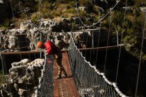 Vue latérale de l'homme caucasien profitant du temps dans la nature, portant un équipement de tyrolienne, regardant vers le bas depuis un pont, par une journée ensoleillée dans les montagnes — Photo de stock